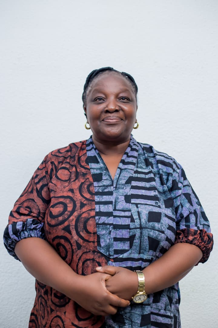 Ashella Tshedza Ndhlovu, in a patterned print dress, photographed against a white wall.