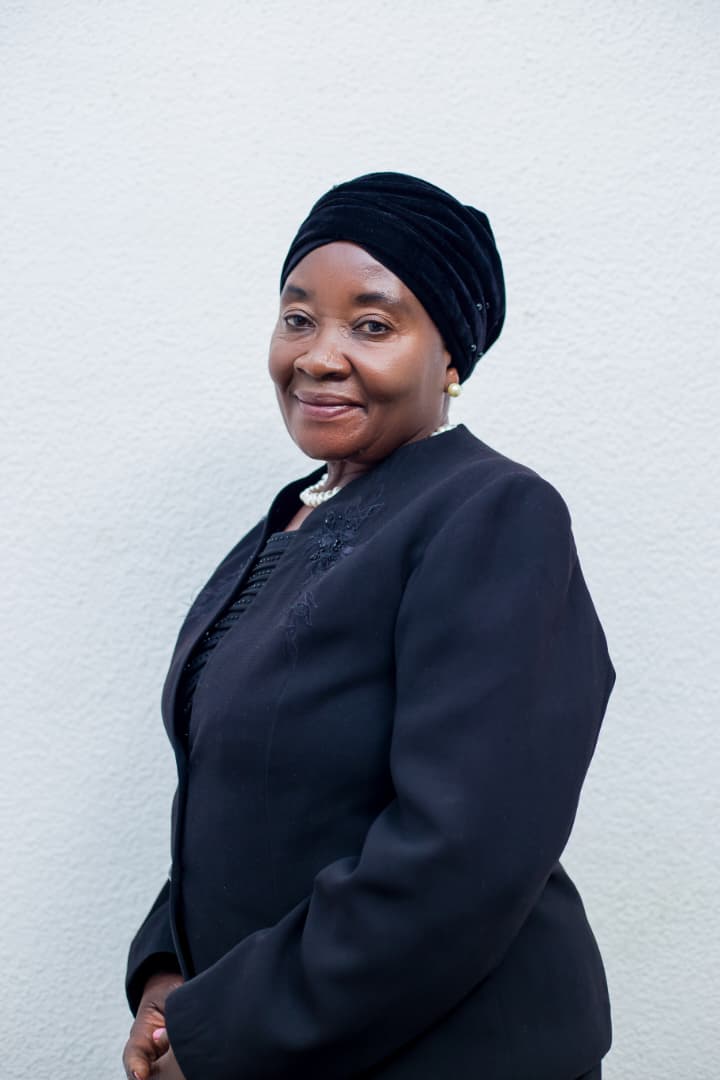Brigadier Gen (RTD) Dr Frida S Kazembe, in a black jacket and headwrap, photographed against a white wall.