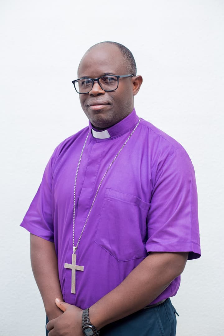 Bishop Japhet Ponda, in a purple clerical shirt with a pectoral cross, photographed against a white wall.