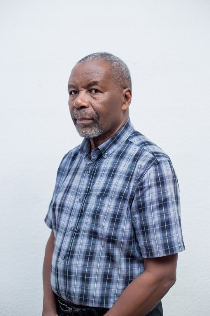 Rev Joe Simfukwe, in a checked short-sleeved shirt, photographed against a white wall.