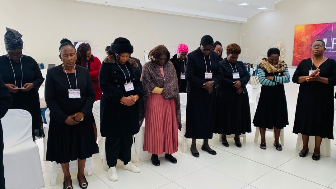 Participants stand together in prayer, hands clasped.