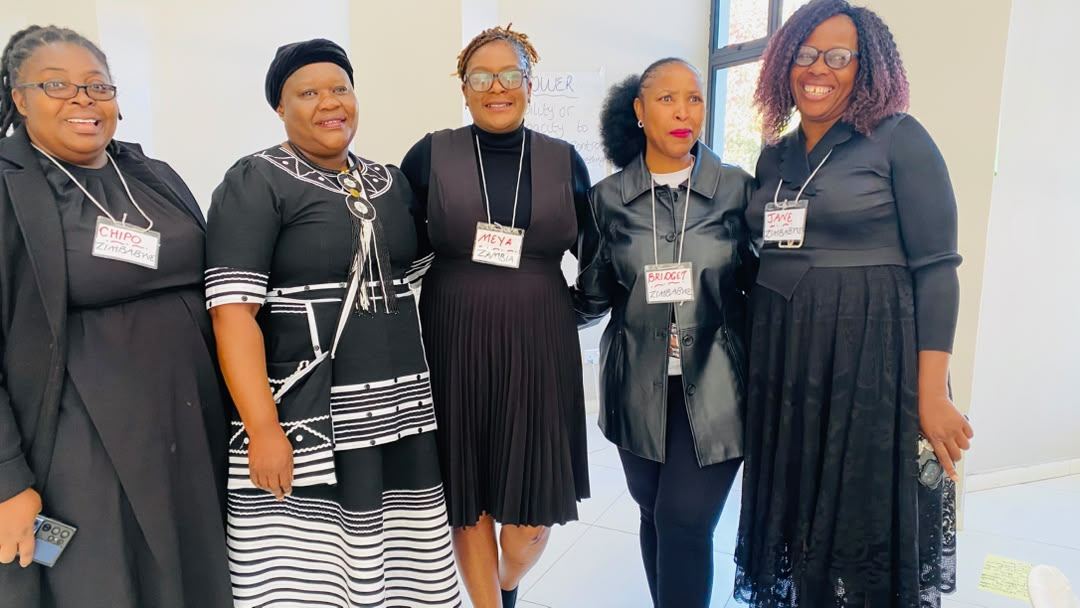 Five participants in black stand together indoors wearing name badges.