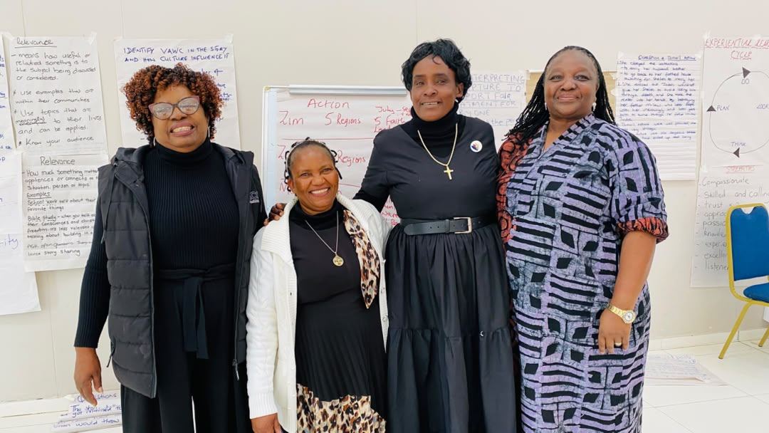 Four participants stand together in front of flip charts recording the group's action plan.
