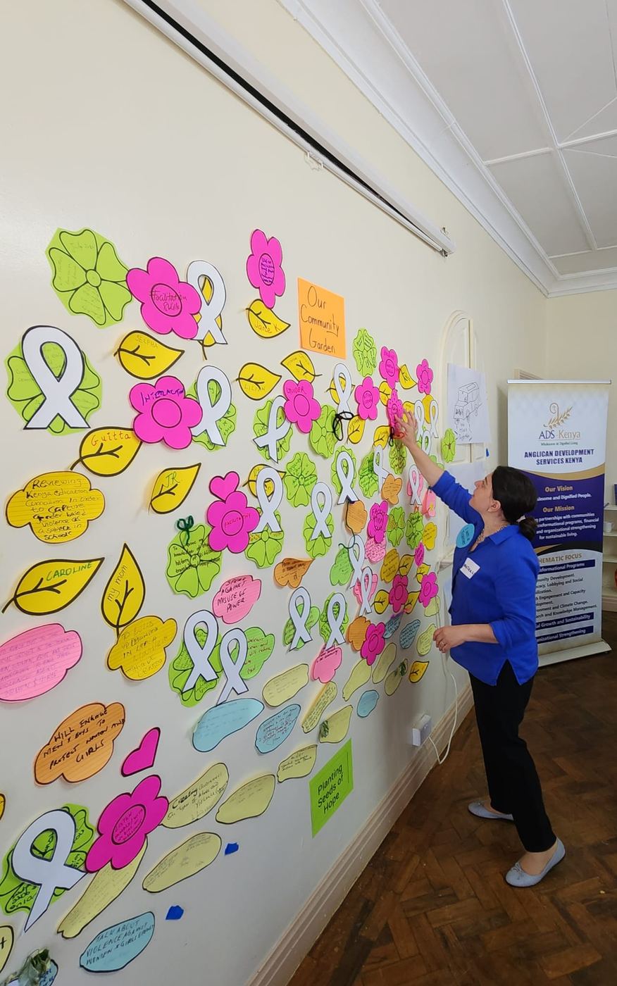 A wide view of a wall covered in hand-drawn paper leaves and flowers, with a participant adding another.